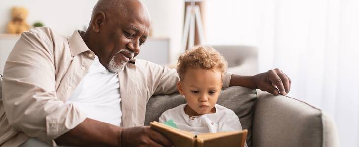 Grandfather reading a book with his granson on the couch