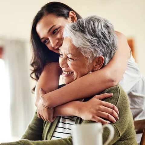 Senior mother hugged from behind by her adult daughter